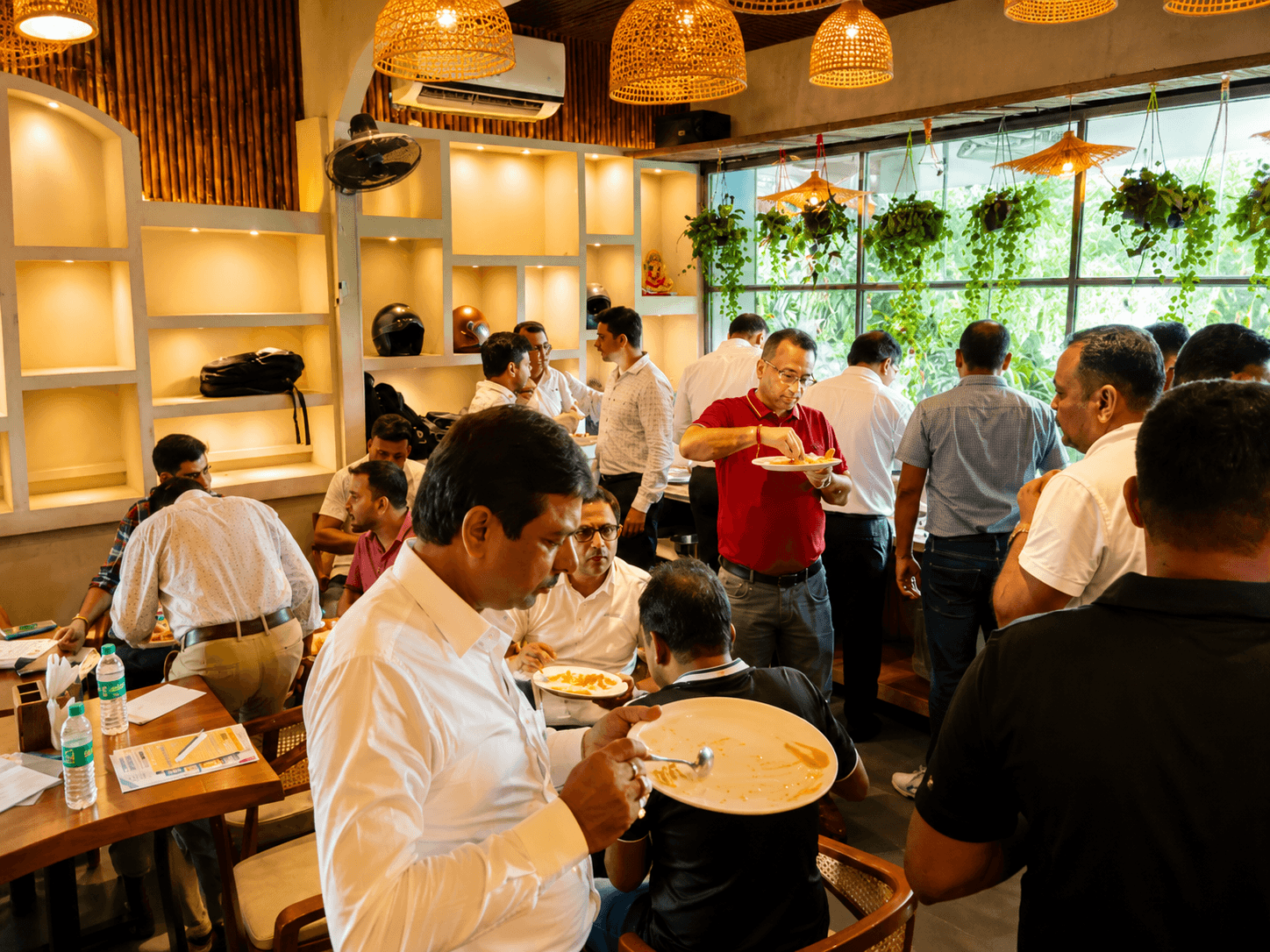People eating in a crowded restaurant with warm woven lamps and lush hanging greenery.