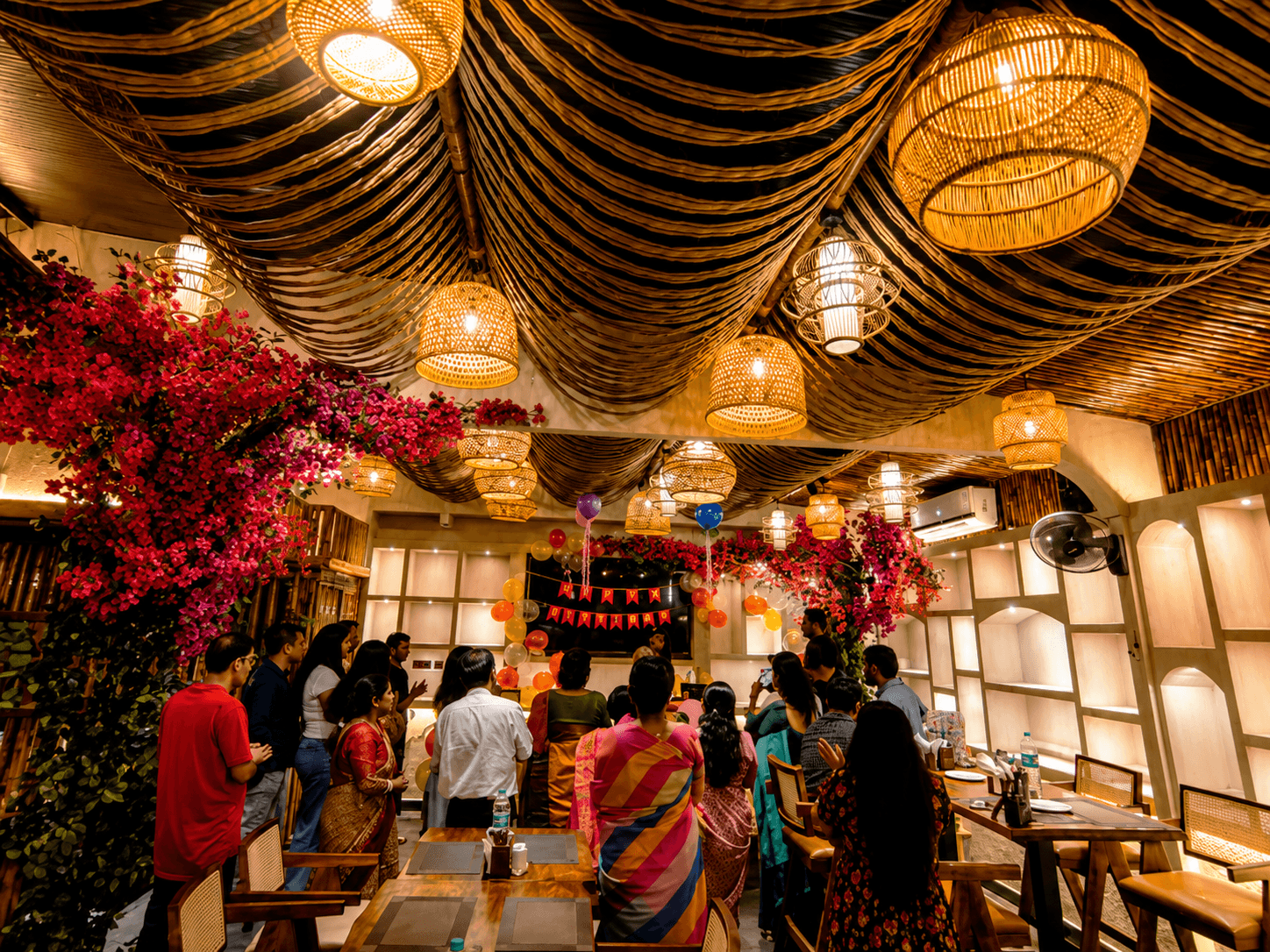 Guests celebrate a birthday in a restaurant featuring woven basket lights and pink bougainvillea.