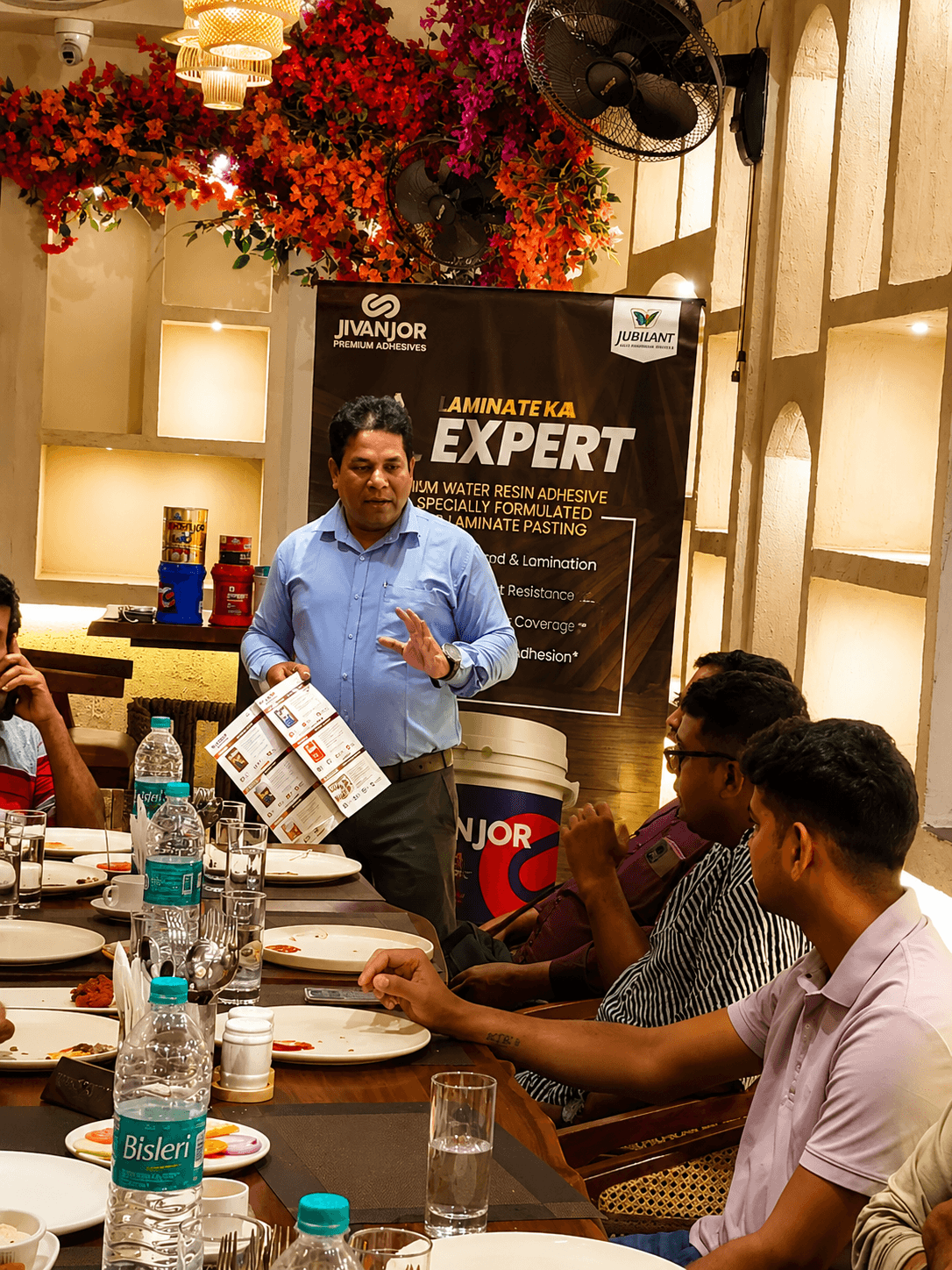 Man in blue shirt presents a brochure to seated guests at a restaurant table.