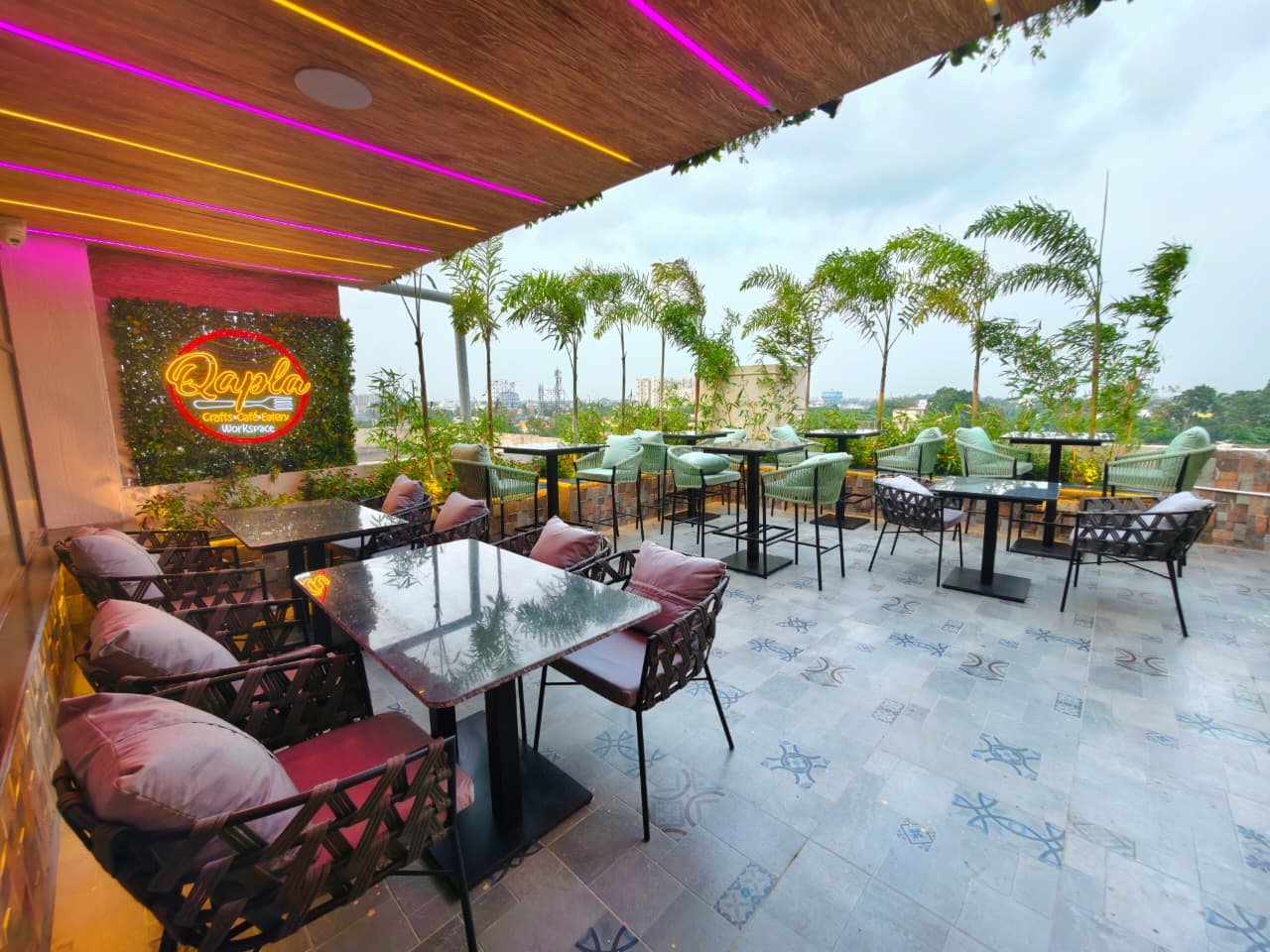 Stylish rooftop cafe with neon lights, modern seating, and palm trees overlooking the city.